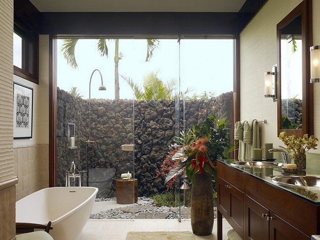 bathroom with open glass wall. stone fence behind the bathroom. white sink ande wooden shelves for towels