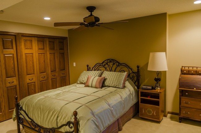 basement bedroom design with dark iron bed frame, brown laminate sideboard lamp, brown varnished wooden door with brown wooden chest of drawers