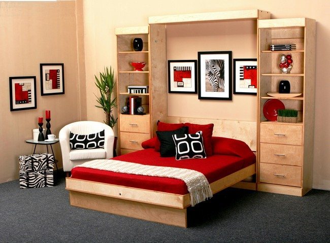 red matrasse on the pine wooden murphy double bed with three pictures and one white armchair