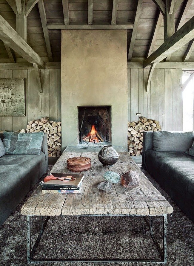 Two long soft sofas with wooden table and live fireplace and woods on the left and grey carplet 