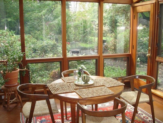 Small sunroom with simple, polished wooden furniture and a beautiful view of the garden
