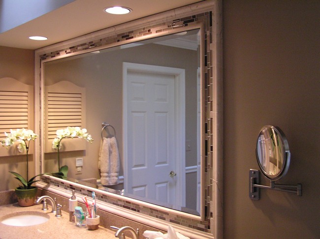 Large mirror encased in a neutral-colored tile frame, with in-ceiling lighting