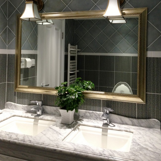 Mirror with neutral-colored frame placed against grey tile in different shades and designs