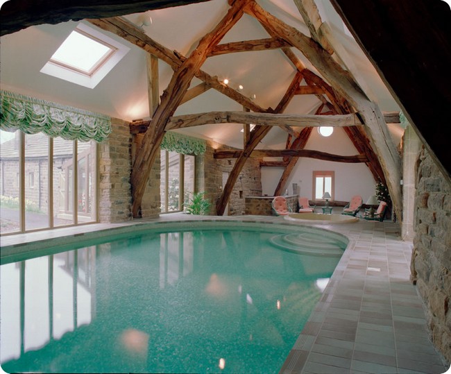 Indoor pool in rustic-style room with wooden beams and stone wall
