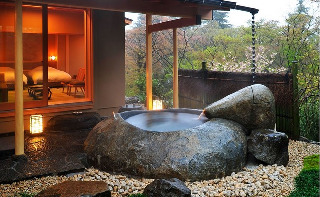 Outdoor tub carved out of a rock, surrounded by pebbles and stone terrace